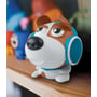 Nærbillede af den søde Muse M-315 DOG Bluetooth-højtaler, siddende på en hylde med andre farverige gadgets i baggrunden.