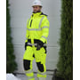 Lyngsøe Rainwear vinterjakke i hi-vis gul og sort bæres af en arbejder udendørs; hætte og refleksstriber ses.