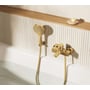 Grohe Lineare kar-/brusearmatur i børstet cool sunrise monteret ved badekar med håndbruser foran en ribbet væg.