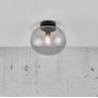 Nordlux Alton loftlampe i røgfarvet glas med sort metal top, vist monteret på et hvidt loft over en rå betonvæg.
