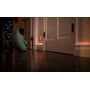 Børns pyjamas med dinosaurer og en bamse ses ved en døråbning, hvor Philips Hue bevægelsessensor tænder lyset langs gulvet.