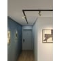 Astro Ascoli Track skinnespots i mat guld lyser fra en sort loftsskinne i en gang med indrammet kunst.