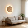 LEDlife væglampe i lyst træ lyser over en sofa i en stue og kaster et varmt skær ud på væggen.