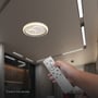 En hånd betjener V-TAC LED-loftslampen med den hvide fjernbetjening, mens lampen lyser i loftet.