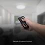 En hånd holder en fjernbetjening til V-TAC LED loftlyset, der bruges til at styre sensorens funktioner i et rum.