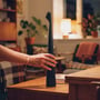 En hånd holder den sorte genopladelige LED-bordlampe på 40 cm på et bord i en hyggelig stue.
