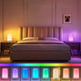 Opladelig RGB+CCT LED bordlampe placeret på et natbord i et soveværelse med dæmpet belysning i forskellige farver.