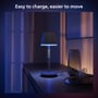 Philips Hue Go bordlampe står på et møbel og lyser blåt, tekst 'Easy to charge, easier to move'.