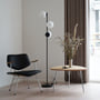 Nordlux Lilly gulvlampe i sort metal med tre opalhvide glaskupler står i et moderne rum ved siden af en stol.