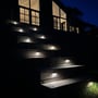 Light By Juul indbygningsspot Saga i sort, diskret integreret i udendørs trappetrin oplyser mørket med varmt lys.