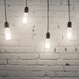 V-TAC 7,5 W LED-pærer lyser i sorte pendelfatninger foran en hvid murstensvæg.