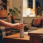 En hånd flytter den hvide, genopladelige LED-bordlampe på et bord i en stue med varm belysning.