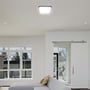 Den firkantede V-TAC LED loftlampe med sort ramme monteret i et moderne stueinteriør med store vinduer.
