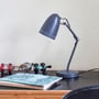 Superliving Dynamo 345 bordlampe i mat sort metal, med justerbar arm og skærm med huller, står på et skrivebord ved siden af bøger og fiskehjul.