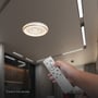 En hånd bruger fjernbetjeningen til den tændte, hvide V-TAC LED-loftlampe i loftet.