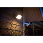 Philips Hue Welcome udendørs projektør lyser på en husmur ved aftenstid, monteret over planter.