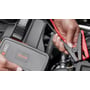 En hånd holder den røde og sorte klemme ved OSRAM BATTERYstart 200 under tilslutning til bilbatteriet.