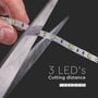 En hånd med en saks klipper i en V-TAC LED strip, der viser en klippelig afstand på 3 LED'er.