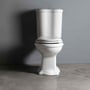 Lavabo Contea Retro gulvstående toilet i hvidt står frontvendt på gråt gulv foran en grå væg.