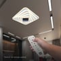Hånd der holder fjernbetjening til V-TAC 150W LED loftlampe, viser kontrolmulighederne for lysstyrke og farve.