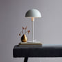 Nordlux Ellen bordlampe i hvid, 40,5 cm, med rund skærm og metalstel, placeret på bøger med en vase.