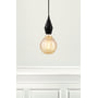 Nordlux Avra square Amber LED-pære med E27 fatning, vist monteret i en sort lampe i et rum med hvid væg og dekorativ panelvæg.