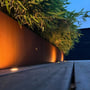Light By Juul S Cosmos indbygningsspots i messing oplyser en udendørs terrasse med planter og rustikke bede ved skumringstid.