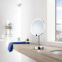 Smedbo Outline makeup spejl med LED-lys og 7x forstørrelse i krom, placeret på en træbordplade ved siden af et håndklæde.