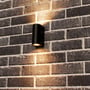 Sort Sacramento udendørs væglampe monteret på en murstensfacade, hvor lampen spreder lys opad og nedad.