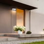 V-TAC LED væglampe monteret på en husfacade med hvidt lys, der belyser indgangen og blomsterdekorationen.