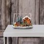 Markslöjd Elta juledekoration i plast med 8 multifarvede LED lys, der forestiller en julelandsby med sne, grantræer og en person.