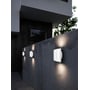 Nordlux Grip Smart hvid LED-væglampe lyser på en betonmur ved et hus, med flere lamper synlige langs muren.