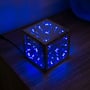 Infinity Cube 15x15 RGBIC tændt med ensfarvet blå belysning på et træbord ved siden af en mørkeblå baggrund.