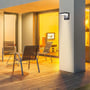 V-TAC LED væglampe monteret på en husmur ved en terrasse, lyser op på en træterrasse med stole.