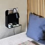 Nordlux Roomi væglampe i mat sort metal med indbygget hylde, USB-port og fleksibelt lampehoved ved siden af en seng.