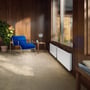 Ebeco Wallflex elradiator 600 WiFi, 400W, 230V, monteret på væg ved et stort vindue i et hyggeligt rum med træpaneler og en blå stol.