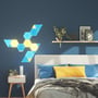 Nanoleaf Shapes Triangles dekorerer en soveværelsesvæg i et blåt og gult mønster over en seng.