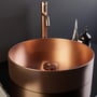 Scandtap Steel Voyage High Amber håndvaskbatteri ses bag en kobberfarvet kumme mod en mørk væg.
