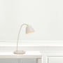 Nordlux Fleur bordlampe i beige metal med messingdetaljer, placeret på et lyst bord med en dekoreret væg bagved.