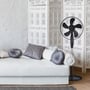 Sort V-TAC stålventilator med fem blade står ved en sofa i et lyst indrettet rum.