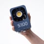 S100-studiebelysning til foto og video, 100 W, holdt i hånden med LED-lyskilden og køleribberne synlige.
