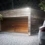 SpectrumLED NOCTIS LUX 3 projektør monteret på en træfacade ved en garage i mørke, lyser op på indkørslen.
