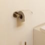 Cosmic toiletpapirholder i børstet guld, monteret på væg med toiletpapir påmonteret.