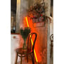 LEDlife Neon Tube LED, 120 cm, gul, står op ad væggen i et caféinteriør og lyser orange.