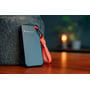 Tæt på Verbatim Pocket SSD i sort, der står op ad en rustik sten, med et orange nøgleringsbånd synligt. En lampe skaber stemningsfuld belysning i baggrunden.