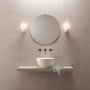 To tændte Astro Lyra Wall Single væglamper i hvidt porcelæn flankerer et rundt spejl over en håndvask.