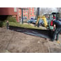 Manuel installation af GreenMax rodbarriere ved en byggeplads, hvor en mand udlægger den sorte HDPE-membran.