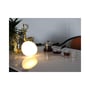 Rund genopladelig RGB+CCT-bordlampe lyser varmt hvidt på et bord med guldsmykkede figurer.