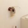 Cosmic toiletpapirholder uden låg i børstet kobber, monteret på lys væg med en toiletpapirsrulle påsat.