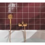 Grohe Lineare kar- og brusearmatur i warm sunset-kobber monteret ved badekar med håndbruser på flisevæg.
